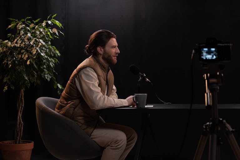 Best podcast hosting - A man sits at a table in a studio setting, recording a podcast with a microphone.